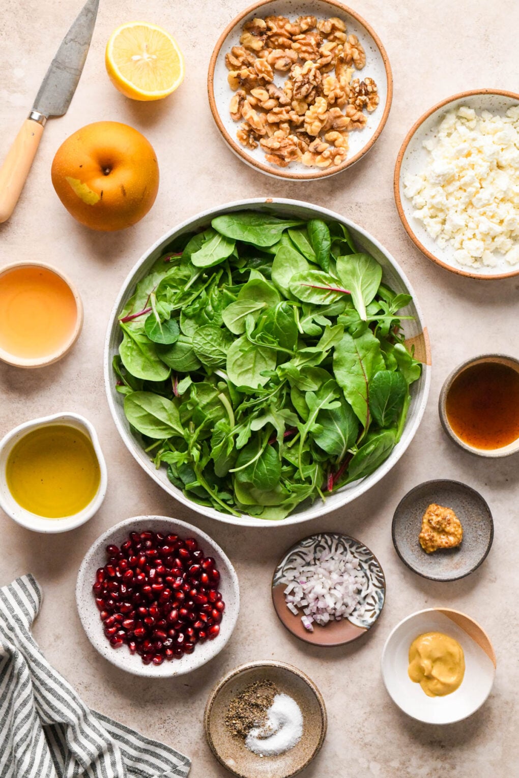 Ingredients for Asian Pear and Walnut Salad with Maple Mustard Dressing on a creamy light brown background in various ceramic dishes.