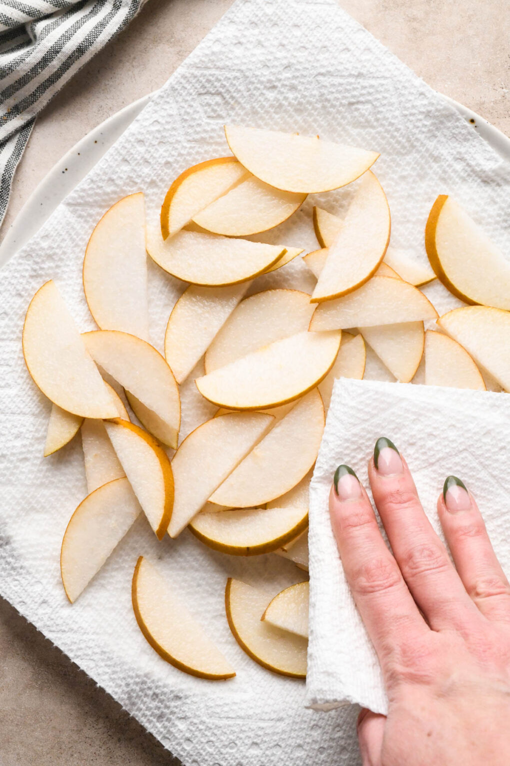 How to make Asian Pear and Walnut Salad with Maple Mustard Dressing: Sliced Asian pears on a large paper towel lined plate, a hand holding another paper towel patting them dry.