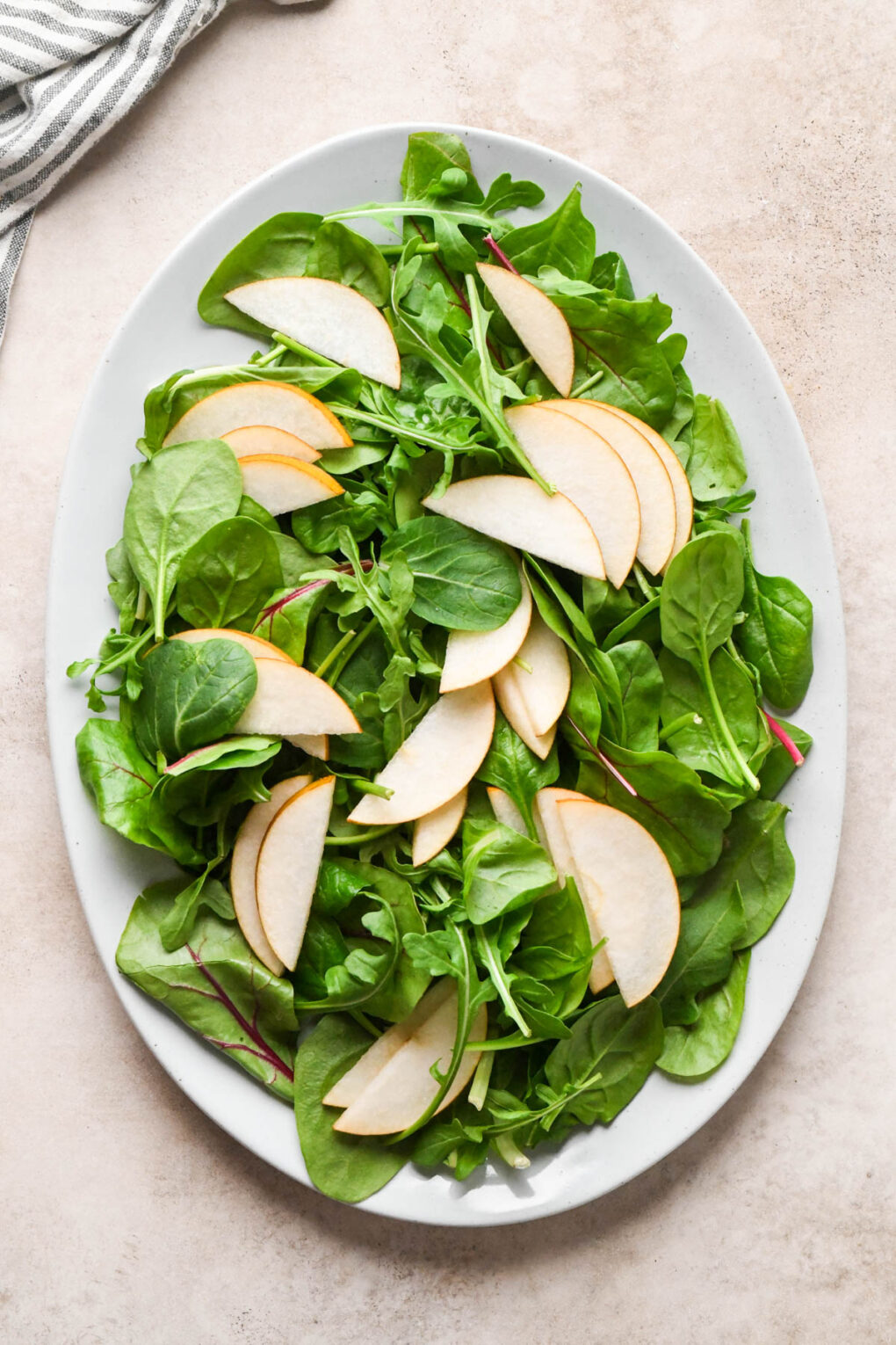 How to make Asian Pear and Walnut Salad with Maple Mustard Dressing: Salad greens and pear slices arranged on a large white oval serving platter.