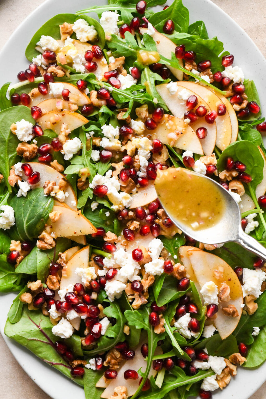 How to make Asian Pear and Walnut Salad with Maple Mustard Dressing: A spoon drizzling maple mustard dressing over the assembled salad.