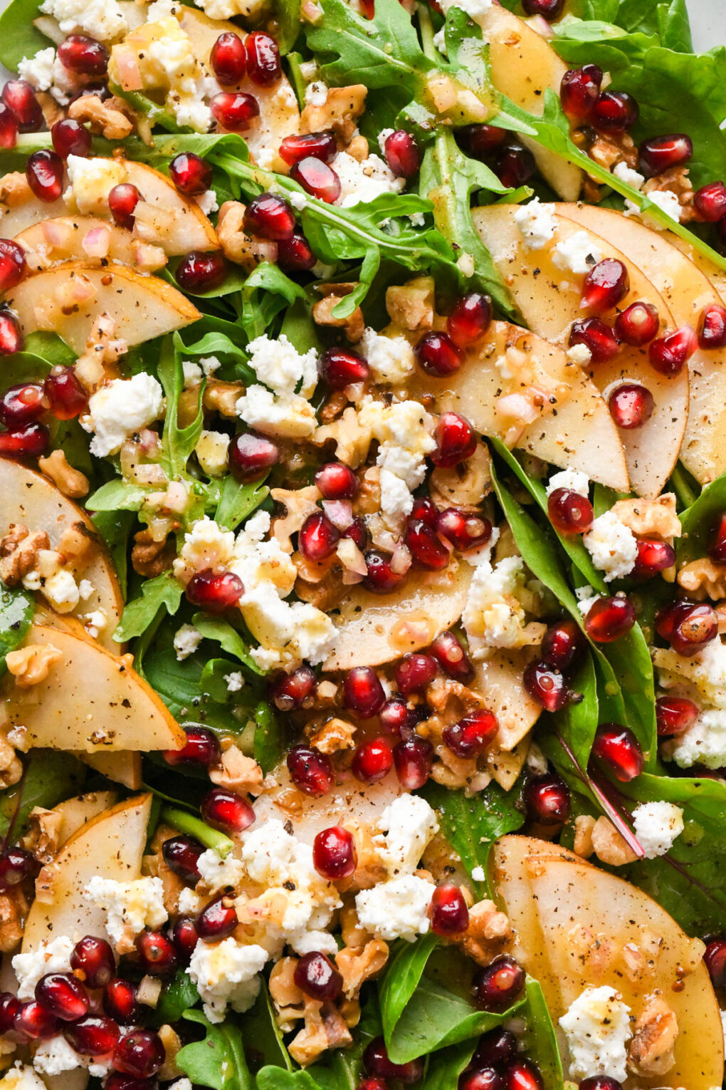 Asian pear salad with tender salad greens, garnished with chopped toasted walnuts, pomegranate seeds, and feta cheese, and drizzled with the dressing.