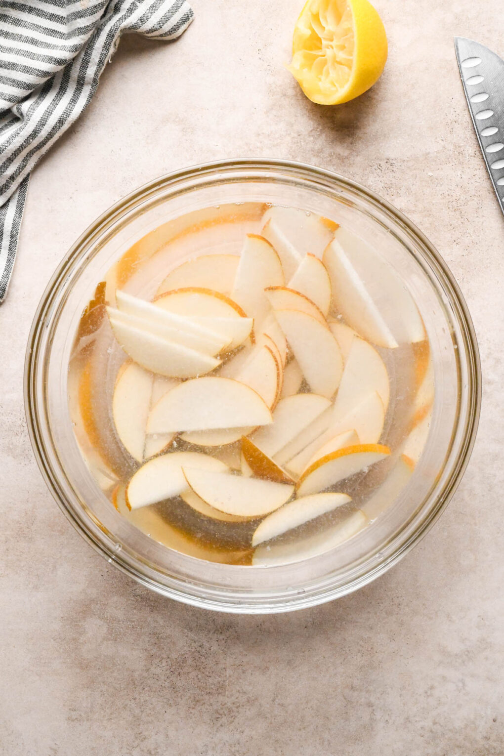 How to make Asian Pear and Walnut Salad with Maple Mustard Dressing: Sliced pears in a large glass bowl of lemon water.