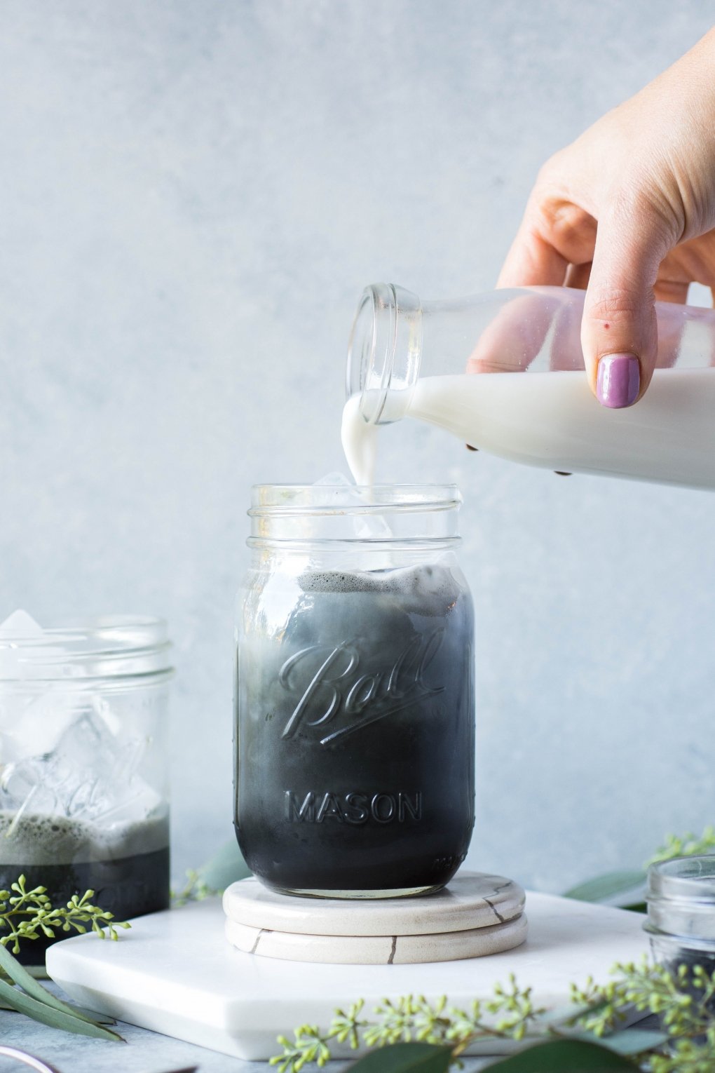 Pouring almond milk into an iced activated charcoal latte.