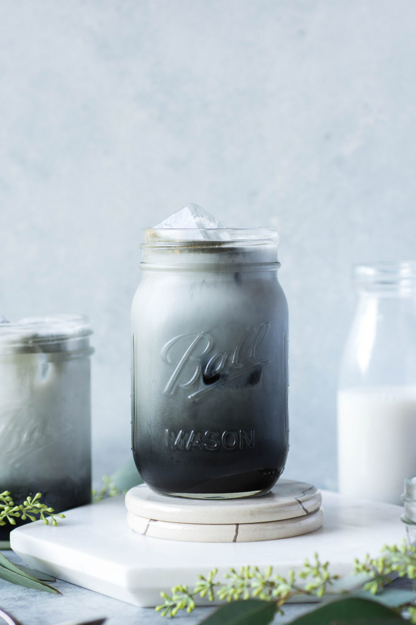 Black and grey toned iced charcoal and almond milk latte in a mason jar, on a grey / blue background.