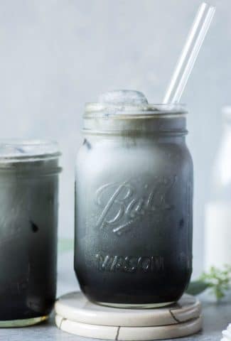 Black and grey toned iced charcoal and almond milk latte in a mason jar, on a grey / blue background.