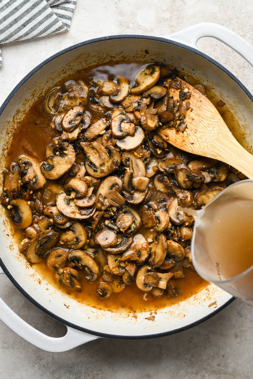How to make Gluten Free Mushroom Gravy: Pouring mushroom broth into skillet with cooked mushrooms.