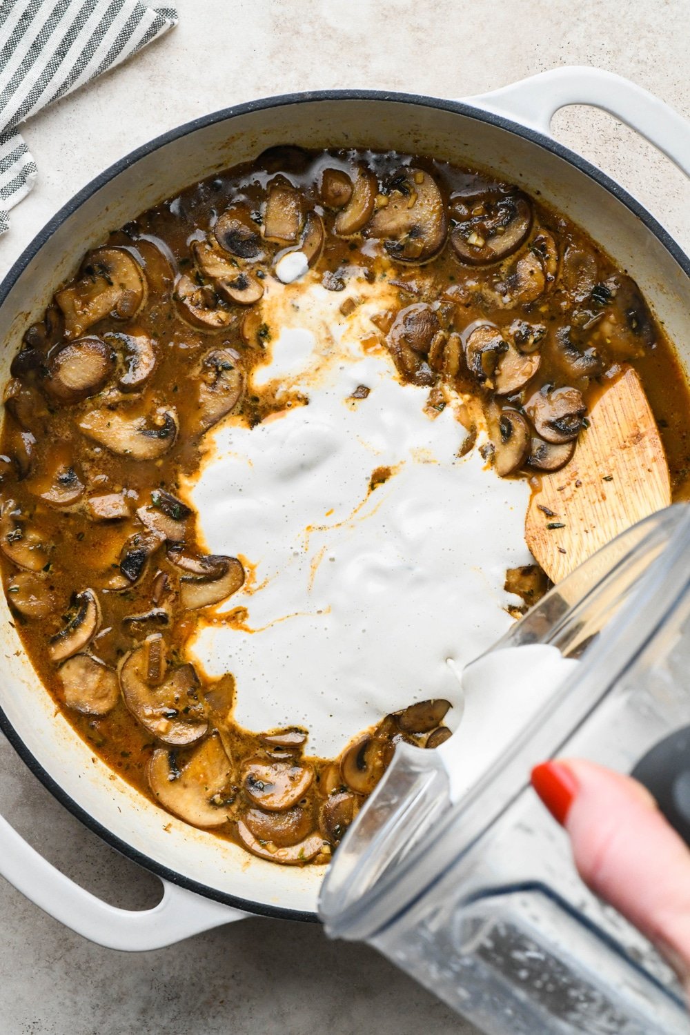 How to make Gluten Free Mushroom Gravy: Pouring cashew cream into skillet with mushrooms and broth.