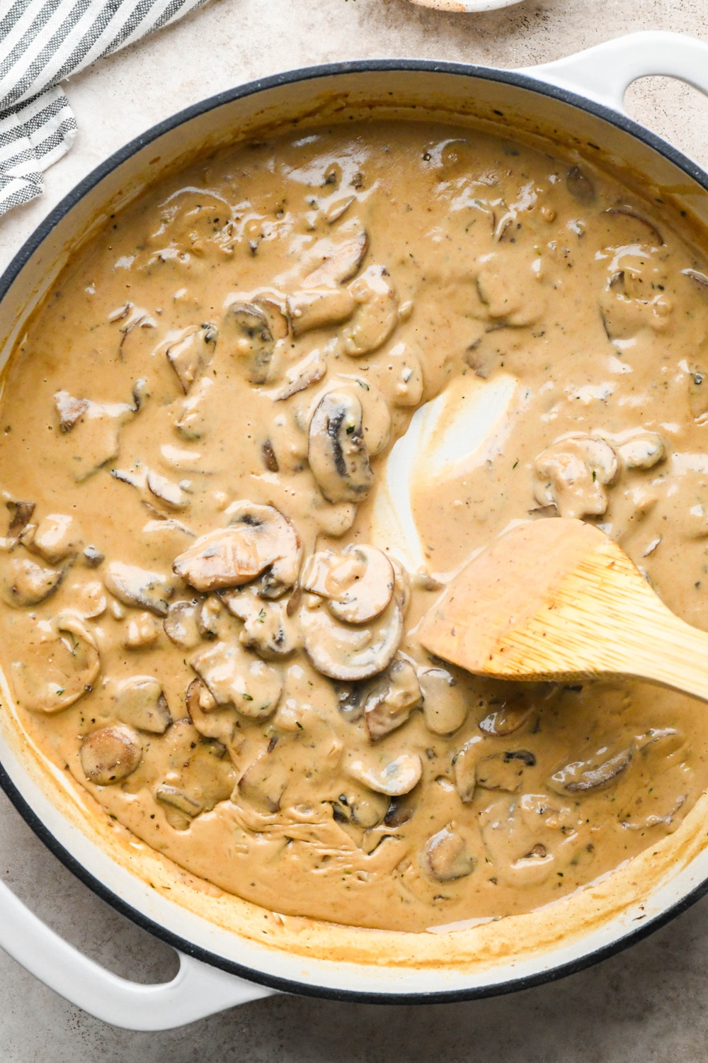 How to make Gluten Free Mushroom Gravy: Mushroom gravy in large skillet with a wooden spatula stirring the gravy around to show the thick and creamy texture.