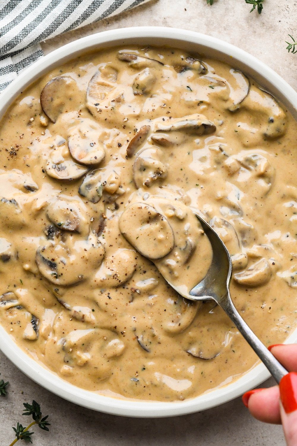 Creamy gluten free and dairy free mushroom gravy in a shallow ceramic serving bowl, with a spoon lifting out a portion of the gravy to show the texture.