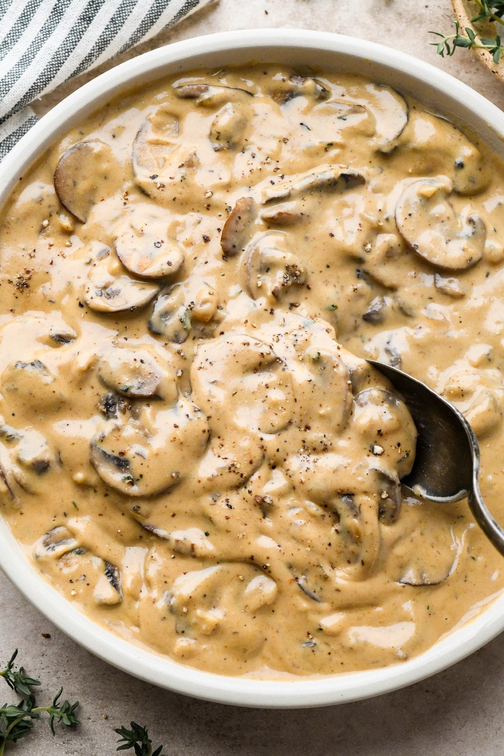 A bowl of thick and creamy gluten free mushroom gravy with a spoon dipping into the bowl to show the texture.