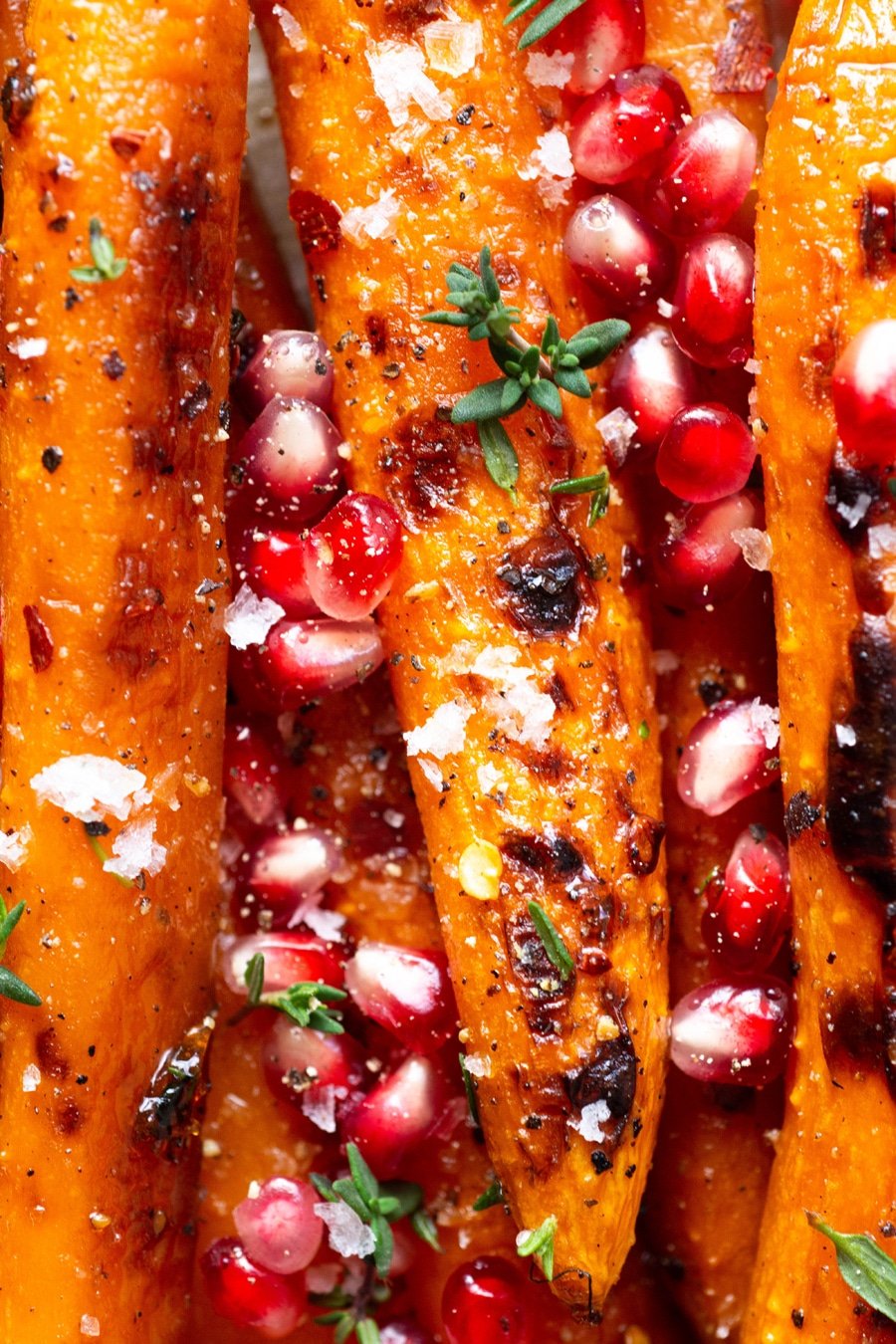 Macro shot of maple chili roasted carrots topped with fresh thyme and pomegranate.