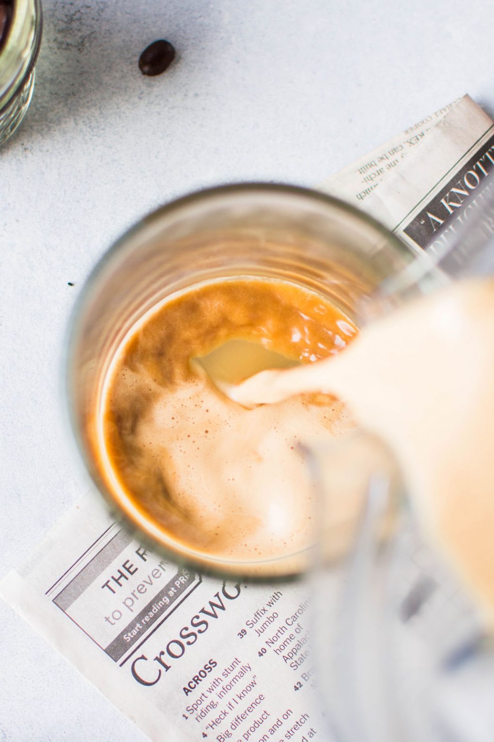 Overhead shot of a blender pouring creamy bulletproof coffee into a glass mug. On a light colored background. 