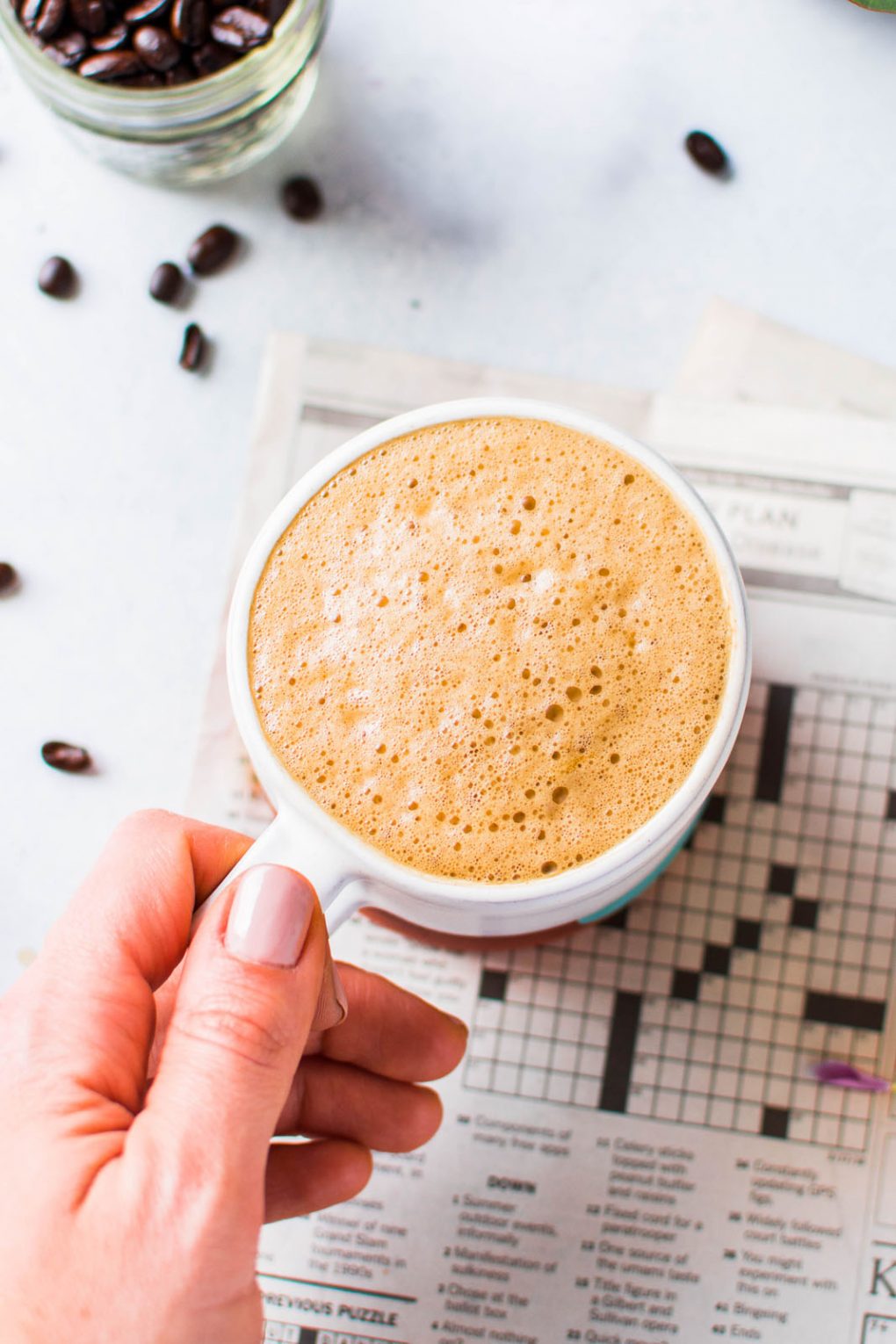 A hand holding a cup of coffee on a light colored background. 