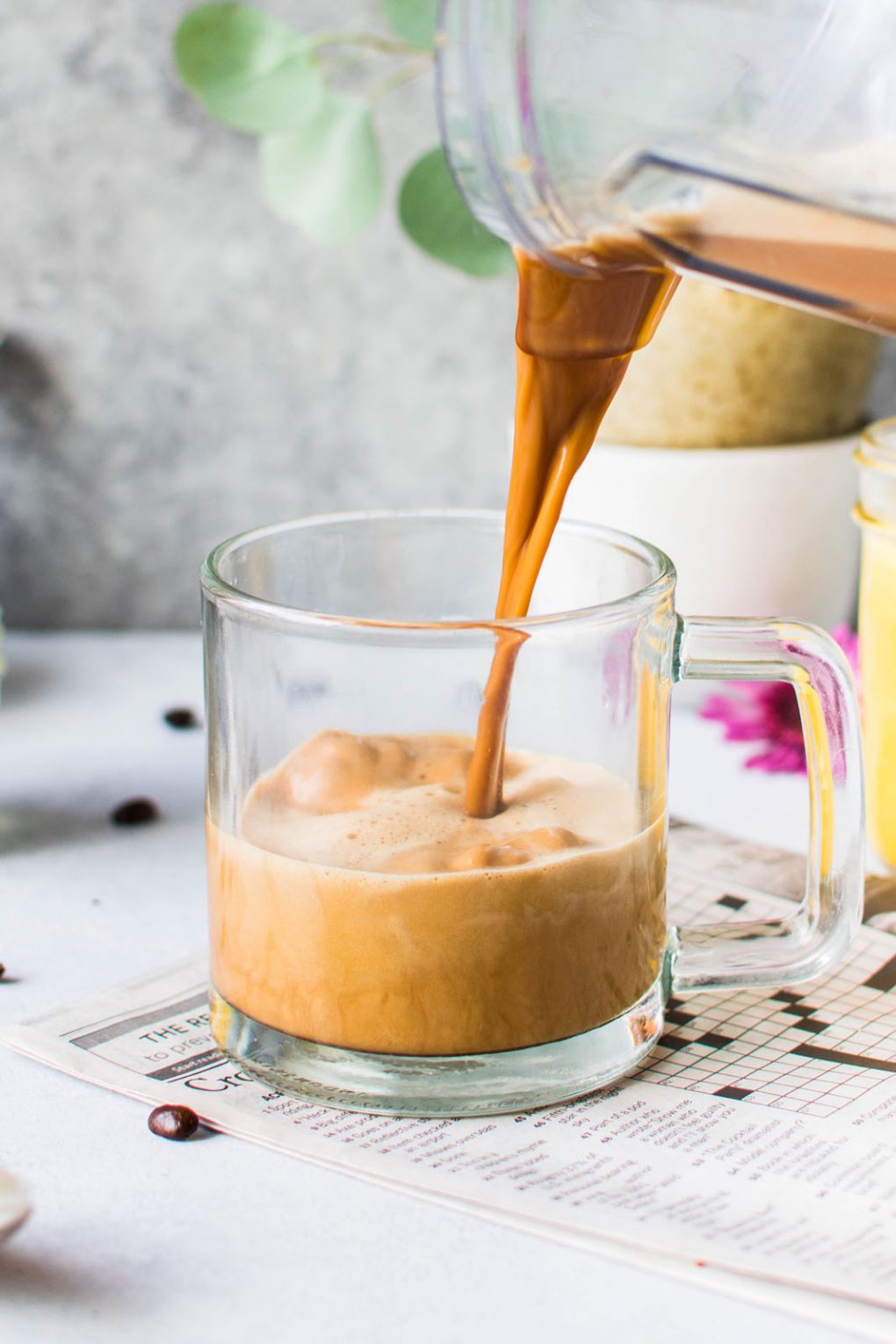 Straight on shot of a blender container just starting to pour super creamy bulletproof coffee into a glass mug.