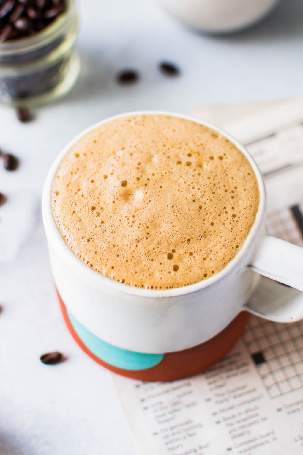 45 degree angle shot of a super creamy cup of bulletproof coffee. On a light background with a newspaper crossword puzzle peeking into the frame. 