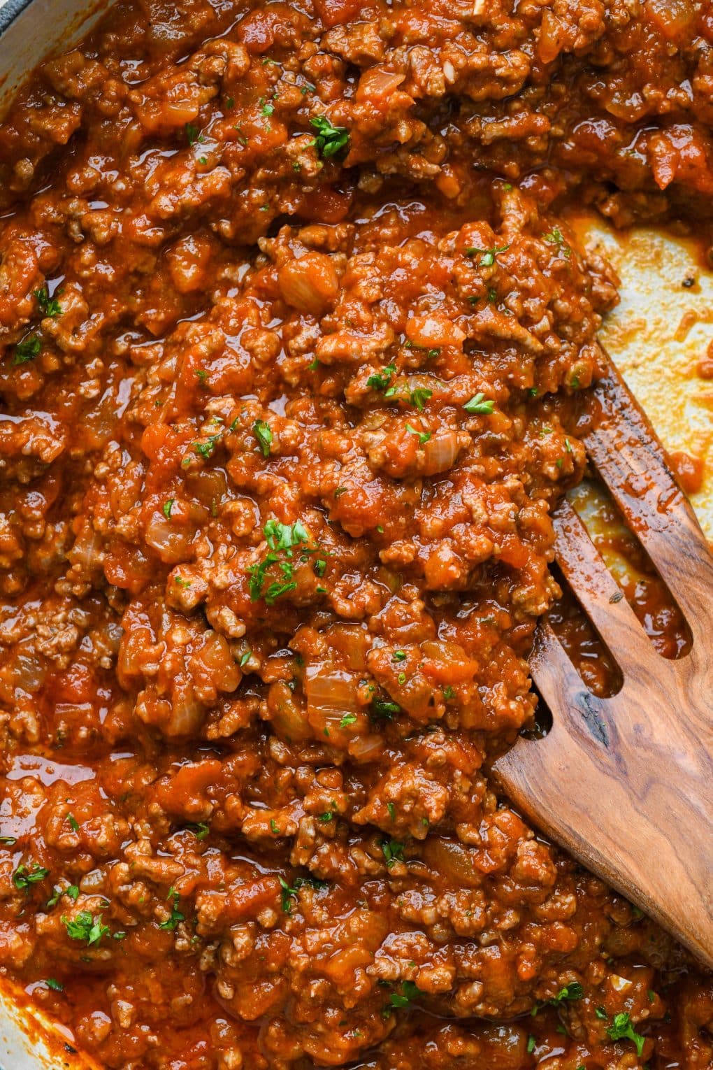 A close up image of a spatula filled with marinara sauce with ground beef, topped with fresh chopped parsley.