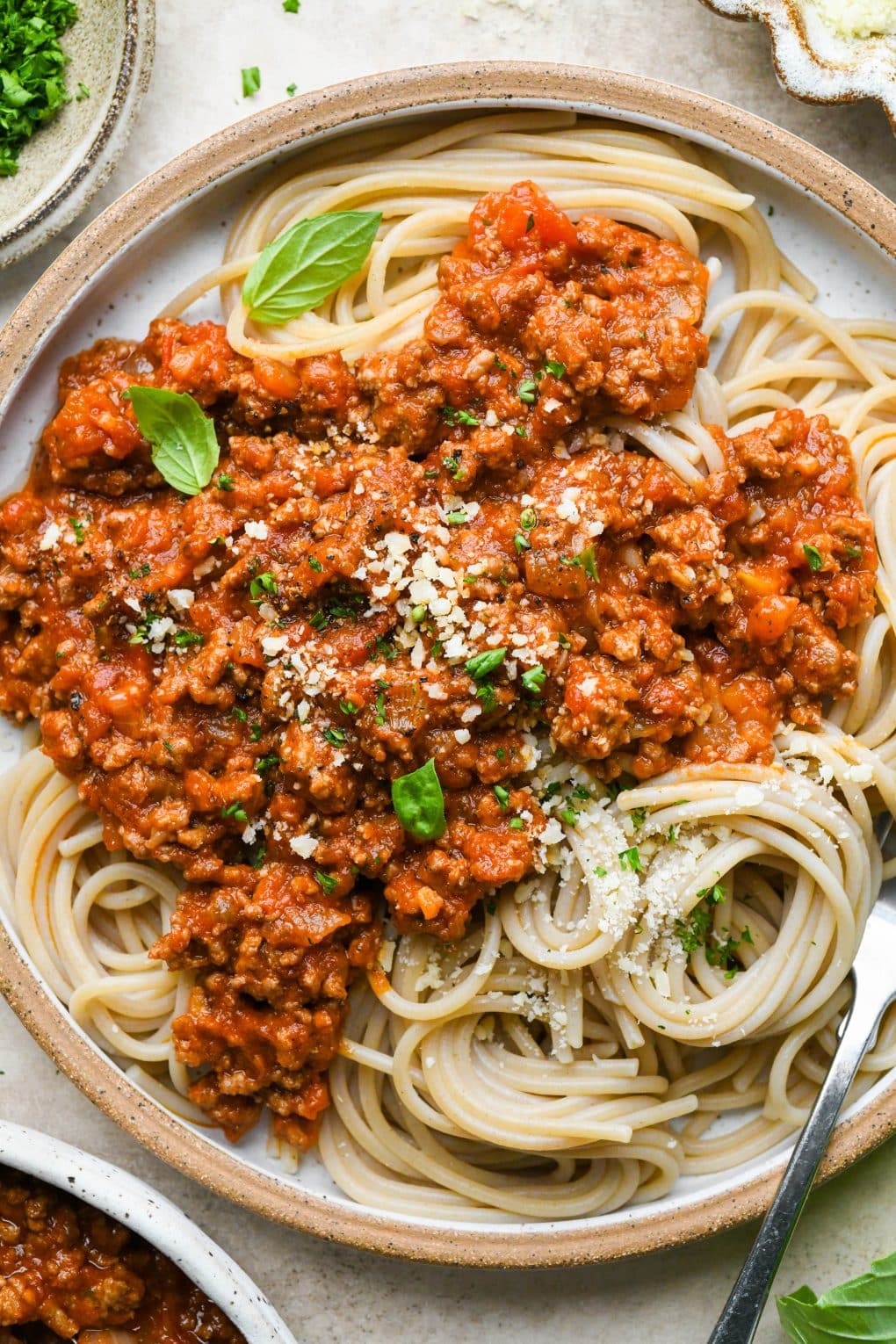 A rustic ceramic plate of twirled spaghetti topped with homemade marinara sauce with ground beef.