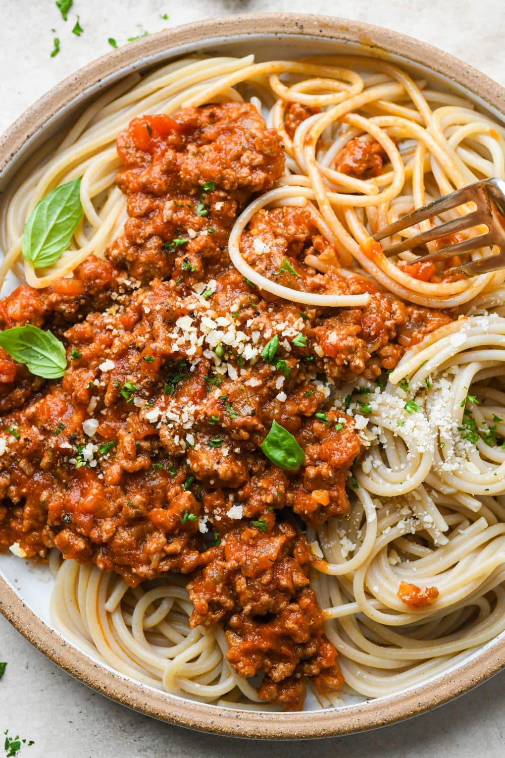 A rustic ceramic plate of twirled spaghetti topped with homemade marinara sauce with ground beef, with a fork twirling some of the noodles.