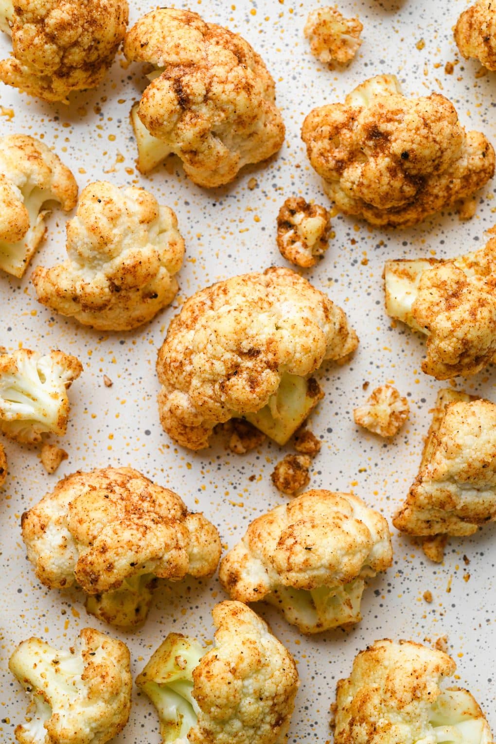 How to make Mexican Roasted Cauliflower: Up close shot of raw cauliflower florets tossed with oil and spices on a baking sheet.