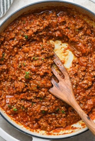 A skillet of marinara sauce with ground beef, topped with fresh herbs.