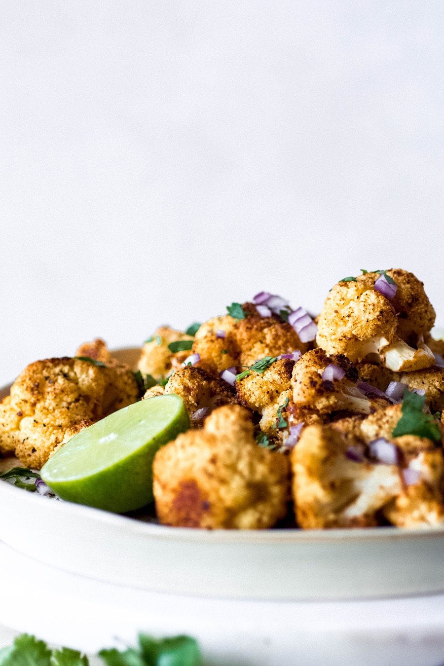 Straight on shot of a plate of mexican roasted cauliflower, topped with chopped red onion, cilantro, and lime wedges.