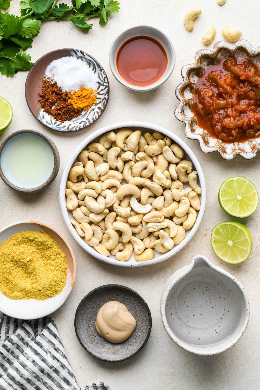 Ingredients for cashew queso in various ceramics on a light cream colored background.