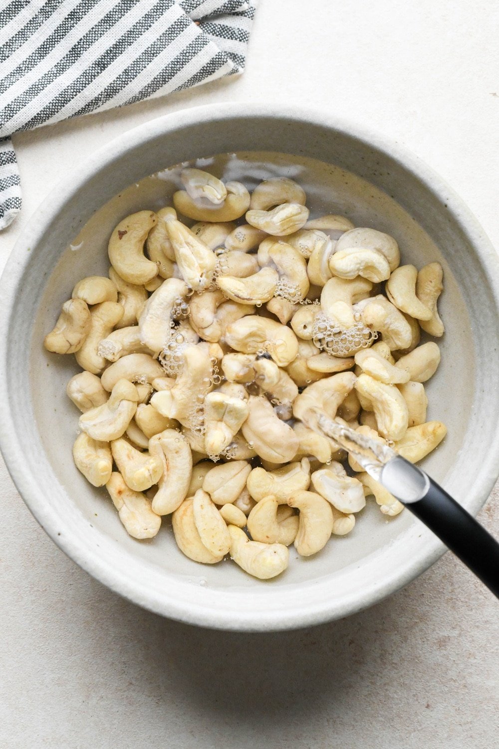 How to make cashew queso: A tea kettle pouring just boiled water into a ceramic bowl of raw cashews to soak.