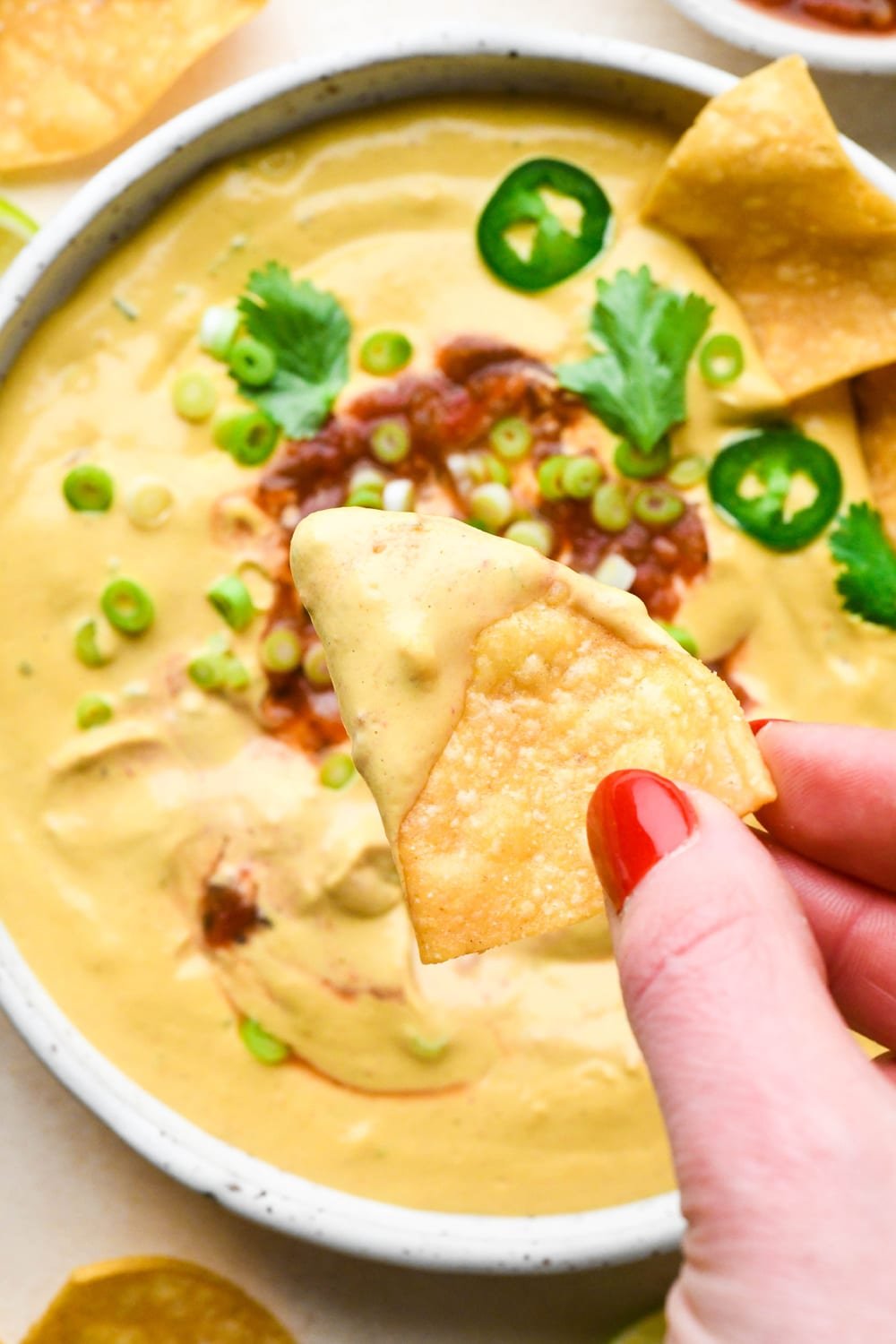 A hand holding a tortilla chip that has been dipped in the cashew queso above the bowl of dip.