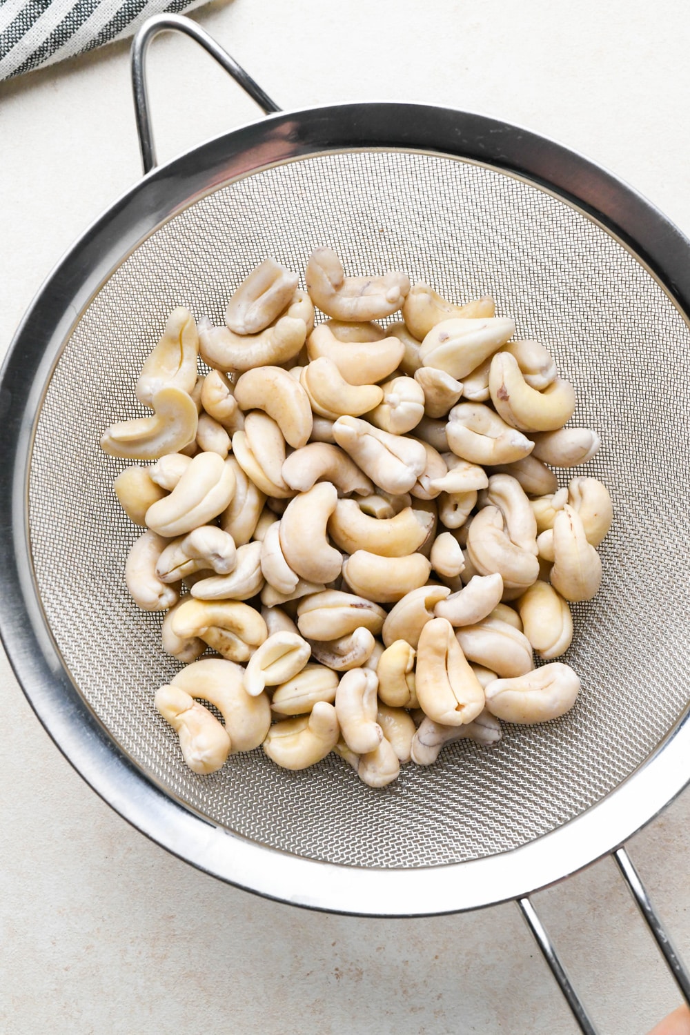 How to make cashew queso: Soaked cashews in a strainer to show the pale color and plump texture.