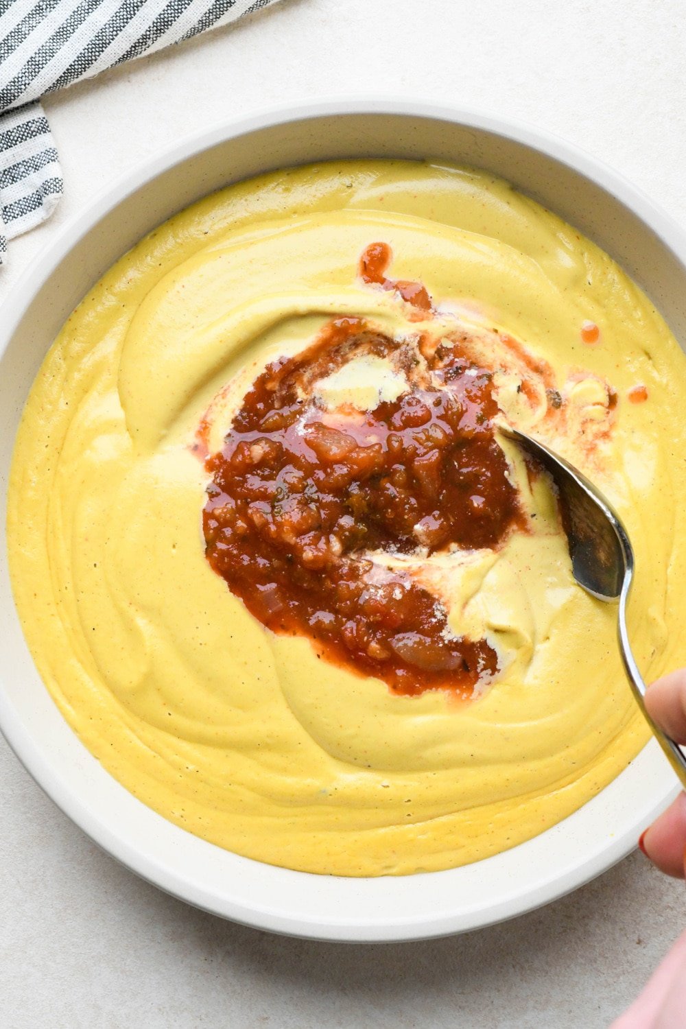 How to make cashew queso: Cashew queso in a shallow ceramic bowl, with salsa before stirred together.