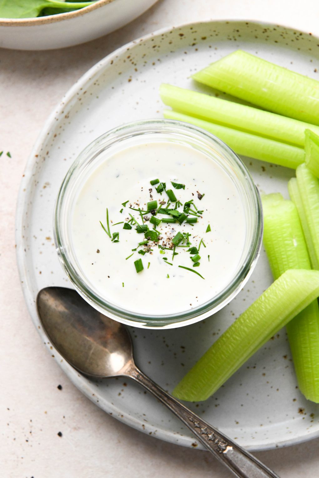 Dairy free ranch dressing in a small glass jar next to celery sticks and a spoon. On a cream colored background.