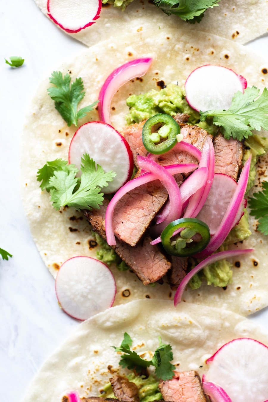 Close up shot of a steak taco on a white background with cilantro, thinly sliced jalapeno, pickled red onions