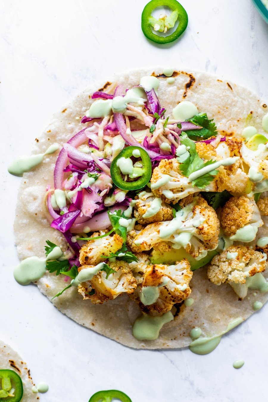 Close up of mexican roasted cauliflower tacos with cabbage slat, sliced jalapenos, and a drizzle of cashew lime crema