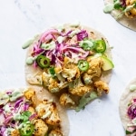 Overhead shot of layered mexican roasted cauliflower tacos with cabbage slaw, sliced jalapenos, and a drizzle of cashew lime crema