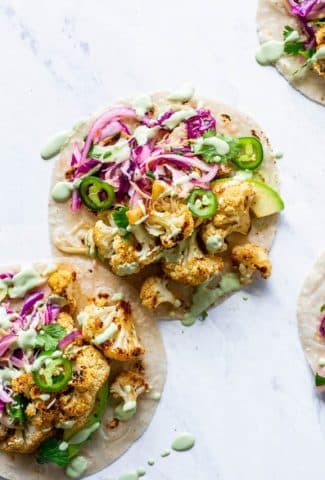 Overhead shot of layered mexican roasted cauliflower tacos with cabbage slaw, sliced jalapenos, and a drizzle of cashew lime crema
