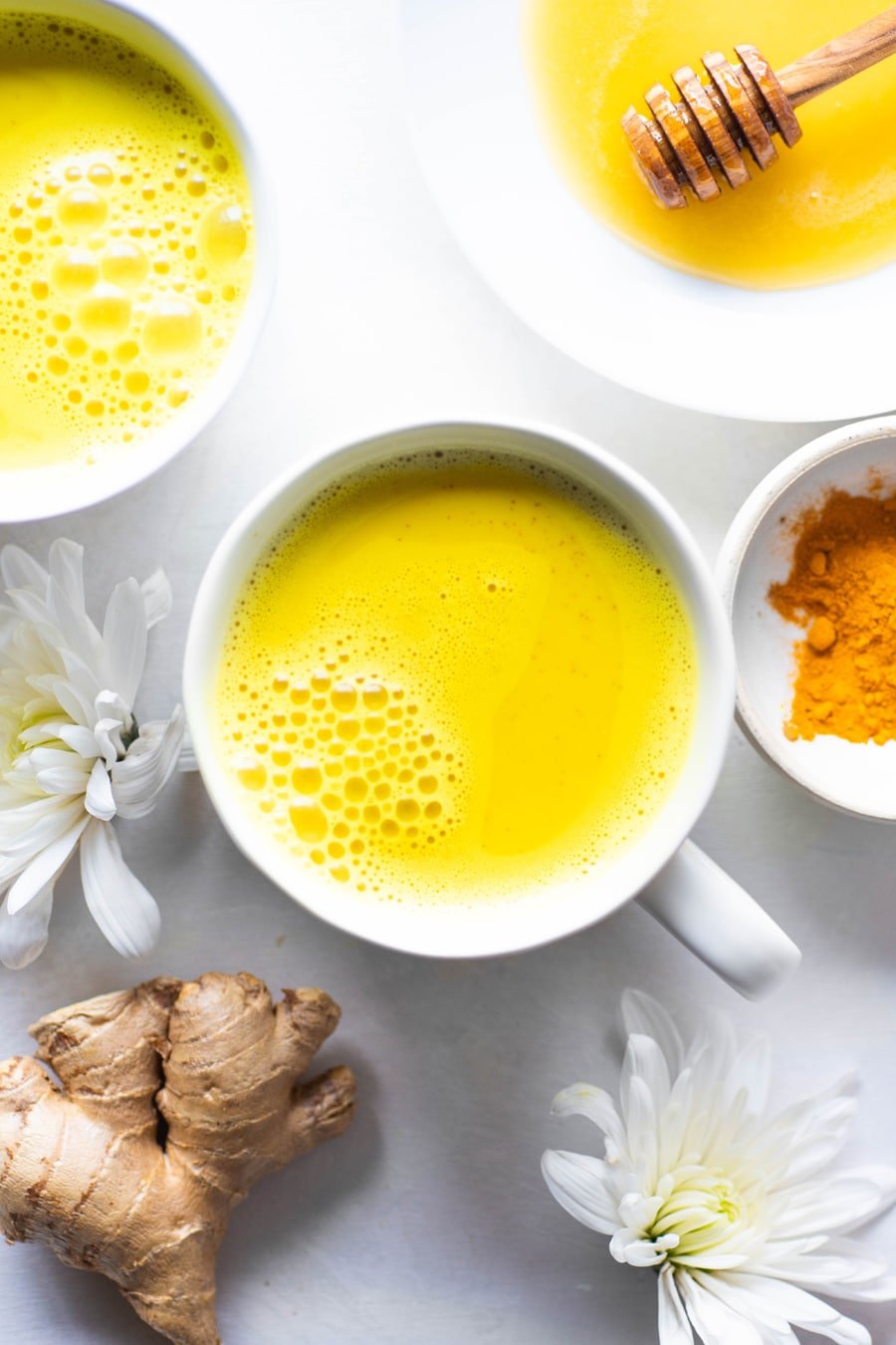 Bright yellow golden milk latte in a white mug with white flowers and fresh ginger