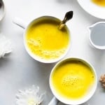 Two bright yellow golden milk latte in a white mug with white flowers and fresh ginger