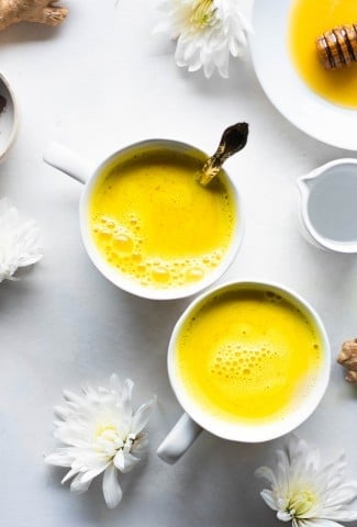 Two bright yellow golden milk latte in a white mug with white flowers and fresh ginger
