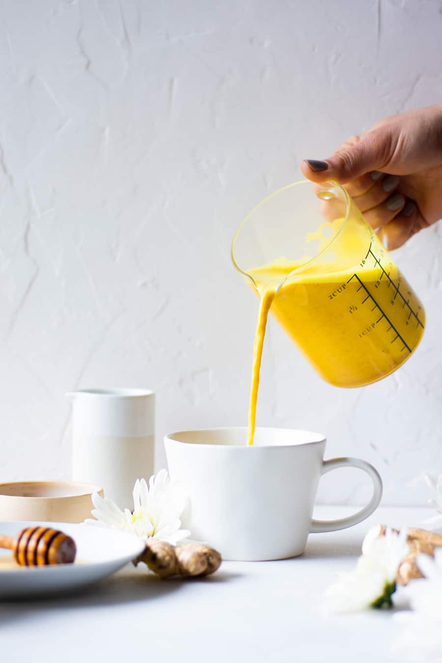 Pouring a bright yellow golden milk latte into a white mug with a white background