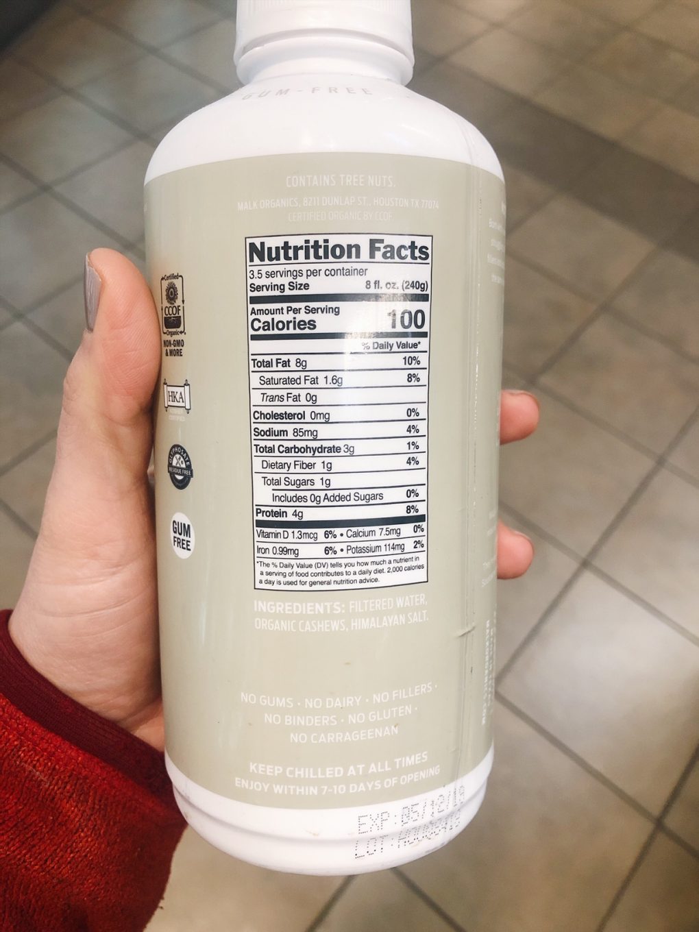 Holding a bottle of malk organics white label with ingredients facing the camera cashew milk in the grocery store