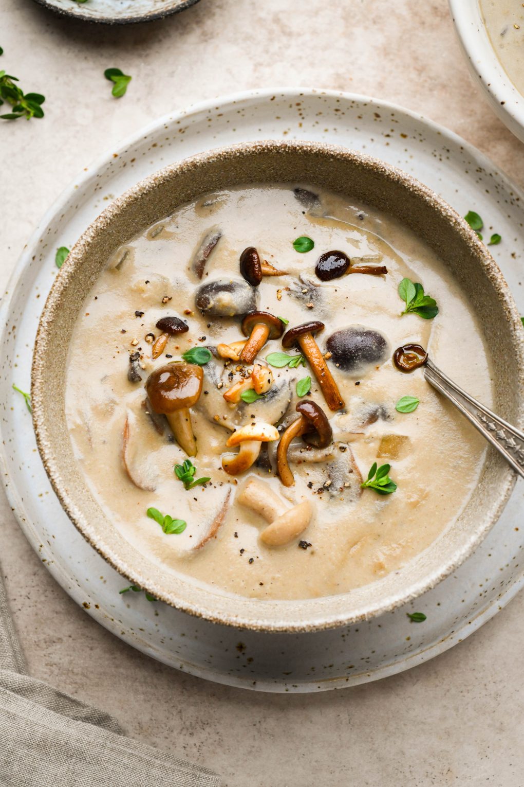 Super creamy homemade cream of mushroom soup in a rustic brown ceramic bowl. Topped with sautéed mushrooms and fresh herbs. 