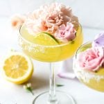 A side view of a bright yellow kombucha margarita served up with a big pink flower and a lime wheel.