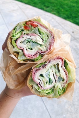 Lettuce wrapped sandwich cut open with turkey, salami, avocado, tomato, and mustard + mayo