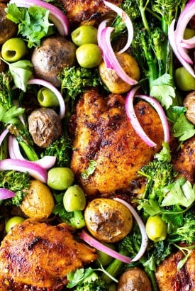 Overhead view of of a roasting tray with spiced chicken thighs, potatos, broccolini, olives, and pickled red onions