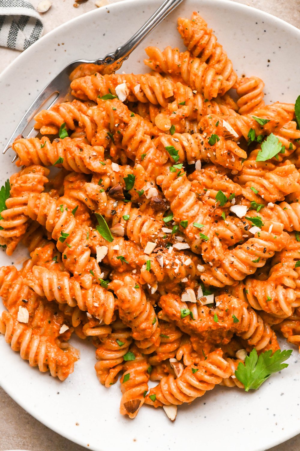 Dairy free and gluten free romesco fusili pasta in a shallow speckled bowl, garnished with chopped almonds and fresh parsley.