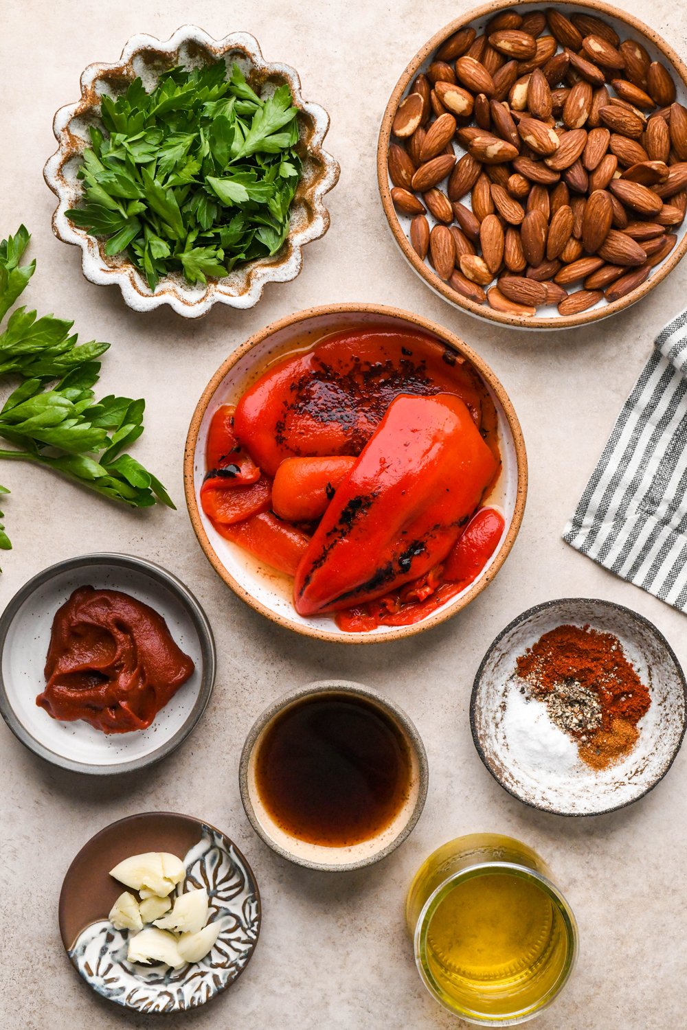 Ingredients for dairy free romesco sauce in various ceramics on a light creamy brown background.