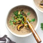 Overhead view of cream of mushroom soup with some sauteed mushrooms and fresh green herbs on top.