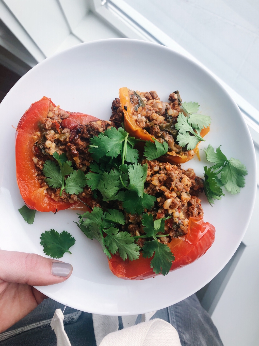Roasted red and orange peppers with ground beef, cauilflower rice, and topped with fresh herbs on a white plate by the window