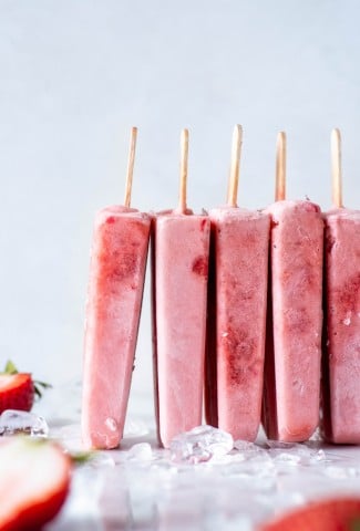 A row of pink strawberry popsicles standing up leaning against each other against a white back drop