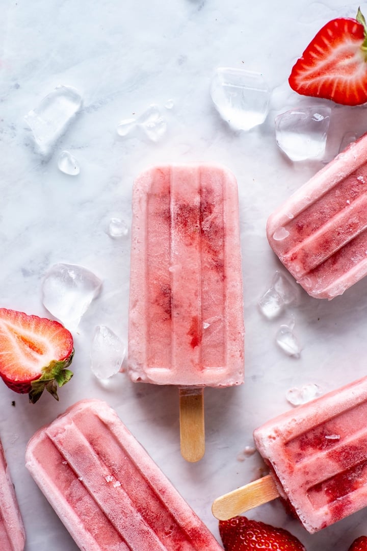 Four scattered strawberry and coconut milk popsicle on a white background